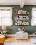 Children's room with green walls, bookshelves, wicker chair, play mat, and wooden rocking chair.