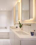 Modern bathroom with marble walls, double sink, illuminated mirrors, bathtub, and a potted plant on the counter.