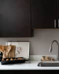 Modern kitchen with dark cabinets, stainless steel faucet, artichokes in a bowl, and wooden utensils on a white countertop.