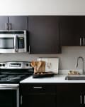 Modern kitchen with dark cabinets, stainless steel appliances, white countertop, and a bowl of artichokes near the sink.