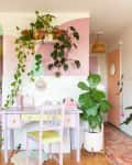 Pastel-themed kitchen and workspace with pink cabinets, green plants, and a lavender desk under a shelf with hanging vines.