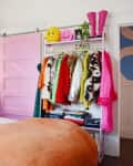 Bedroom with pink door, lush green wall decor, colorful clothes rack, and a bed with orange bedding.
