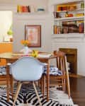 Mid-century dining room with wooden table, zebra rug, white chair, and built-in shelves filled with books and decor.