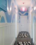 Blue hallway with wavy white patterns, black and white geometric rugs, and a pink ceiling light.