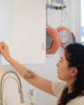 Person with a tattoo opening a kitchen cabinet, revealing bowls inside, with hanging pots in the background.