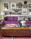 Eclectic living room with purple sofa, colorful wall art, patterned coffee table, and blue chair on a vibrant rug.