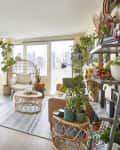 Bright living room with wicker furniture, large mirror, plants, and city view through windows.