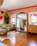 Living room with green velvet sectional, large mirror, wooden dresser, abstract wall art, and colorful stained glass windows.