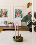 Dining room with sewing machine, vibrant plant decor, orange chairs, and framed skeleton artwork on the wall.