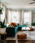 Living room with teal sectional sofa, colorful cushions, poufs, plants, and a light blue door.
