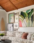 Living room with patterned sectional sofa, round coffee table, wall art, woven baskets, and a surfboard decor piece.