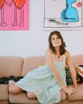 Woman in a light dress sitting on a beige sofa with colorful pillows, surrounded by quirky wall art.