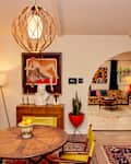 Mid-century modern living room with a round wooden table, yellow chairs, art pieces, and a large archway leading to a cozy seating area.