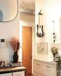 Hallway with wall-mounted guitars, a round mirror, plants, books, and a wooden cabinet.