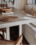 Cozy dining nook with a beige sectional, checkered pillow, woven placemat, and wooden bowl on a concrete table.