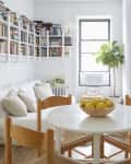 Cozy kitchen and living area with a round table, wooden chairs, bowl of lemons, white sofa, and wall-mounted bookshelves.