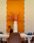 Dining table with brown chairs, blue cups, and a white vase with dried branches against an orange accent wall.