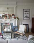 Living room with a fireplace, books, framed art, two chairs, a plant, and a motivational poster on the wall.