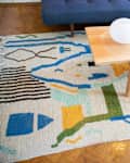 Colorful abstract rug under a wooden coffee table with books, a candle, and a vase of pink flowers.