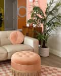 Retro living room with cream sofa, orange and pink pillows, peach ottoman, and vibrant yellow and pink walls with geometric patterns.