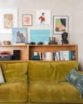 Olive green sofa with cushions, wooden shelf with books, art, and decor, including a bust and vintage cameras.
