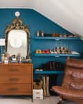 Dressing room with teal walls, vintage mirror, wooden dresser, brown leather chair, and shelves of shoes and clothes.
