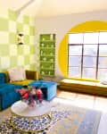 Living room with green and yellow checkered walls, colorful modular sofa, round window, and floral centerpiece on a coffee table.