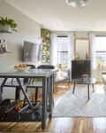 Open living room with a green sofa, large potted plant, wall art, and a view into a bright bedroom.