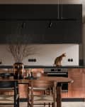 Modern kitchen with copper cabinets, black upper cabinets, a cat on the counter, and a dining table with a vase and chairs.