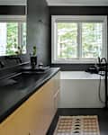 Modern bathroom with black walls, large windows, a white bathtub, black fixtures, and a wooden vanity with a black countertop.