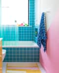 Brightly colored bathroom featuring yellow tiled vanity, turquoise wall tiles, a white bathtub, and a pink accent wall.