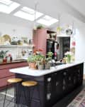 Modern kitchen with pink cabinets, marble island, plants, and a dining table, featuring a large pendant light and colorful decor.