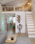 Loft-style living room with a gray sofa, wall art, plants, and a wooden staircase leading to an upper level.