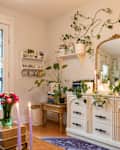 Cozy living room with plants, candles, a vintage dresser, and a large mirror reflecting greenery.