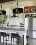 Modern kitchen with white cabinets, stainless steel appliances, black pendant lights, and a large island with bar stools.