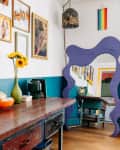 Eclectic dining room with a large purple mirror, wooden table, sunflowers, and colorful wall art.