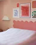 Bedroom with pink scalloped headboard, pastel walls, blue desk, and colorful wall art.