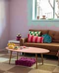 Living room with pastel walls, brown sofa, colorful pillows, pink coffee table, and a wall-mounted TV above a fireplace.