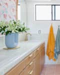Bright bathroom featuring a light wood vanity, colorful towels, and a glass shower with gold fixtures.