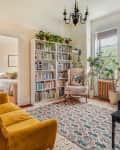 A white bookcase along the far wall of a room with a large rug and a black piano.