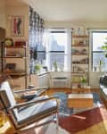 Bright living room with a green sofa, modern chair, wooden coffee table, plants, and wall art, featuring large windows.