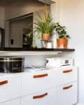 White sideboard with leather handles, topped with a printer, black tin, and potted plants on a shelf above.