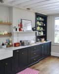 Bright kitchen with dark cabinets, open shelves, farmhouse sink, and a wooden dining table by a large window.