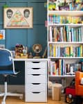 Home office with blue panel walls, white desk, blue chair, bookshelf filled with books, and an orange armchair with plush toys.