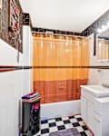 Bathroom with orange shower curtain, black and white checkered floor, white vanity, and framed artwork on the wall.