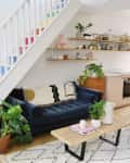 Living room with blue sofa, wooden coffee table, plants, and open kitchen under rainbow staircase.