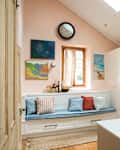 Kitchen with a blue cushioned bench, colorful pillows, stainless steel fridge, and a counter with flowers and fruit.