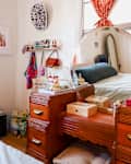 Bedroom with a wooden vanity, round mirror, decorative items, and a bed with a blue pillow. Art and shelves on the wall.