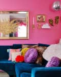 colorful living room with some pink walls, some white, pink front door, blue velvet sofa with colorful throw pillows, arched deco mirrors, lots of colorful framed wall art