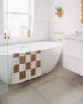 white bathroom with tiled walls, white freestanding tub, and brown and white checkered bath mat
